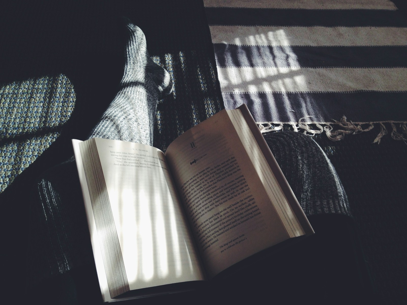 Book on lap. Image shows only the book with stockinged feet sticking out from underneath. The vibe is cozy and dreamy.
