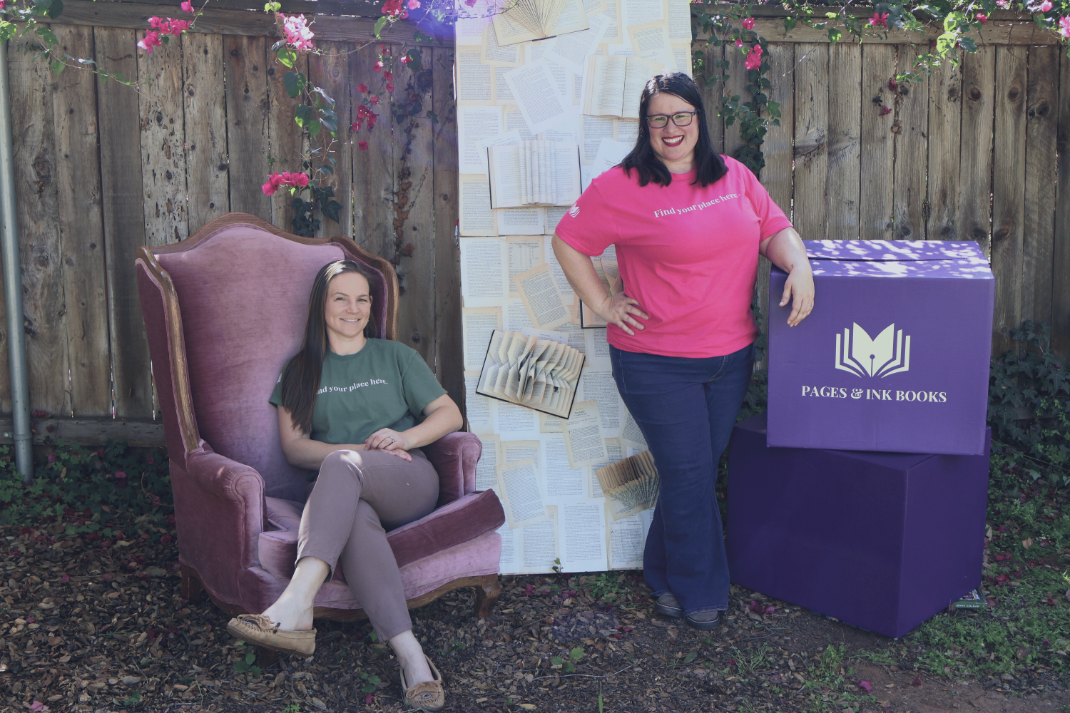 The co-founders of Pages & Ink books pose next to a book wall and a box with their logo on it.